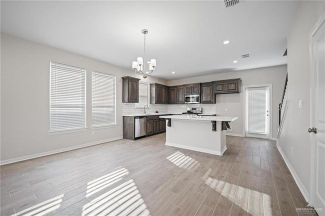 Kitchen with stainless steel appliances, a chandelier, dark brown cabinets, light countertops, and light wood finished floors | Image 4