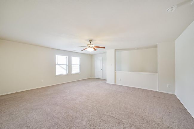This spacious game room features neutral carpeting, a ceiling fan, and ample natural light from two windows. The open layout offers versatility for various furniture arrangements. | Image 19