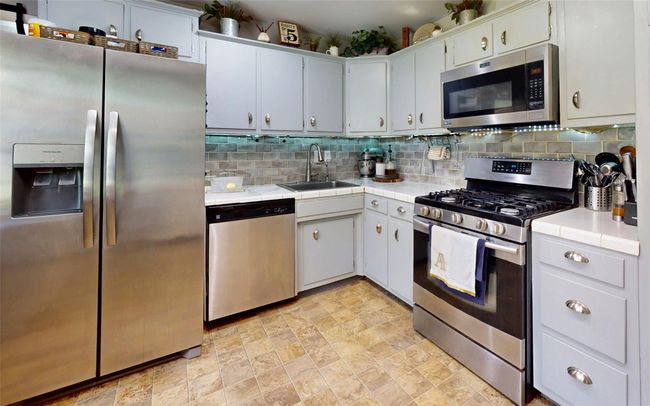 Kitchen with stainless steel appliances, a sink, decorative backsplash, and tile counters | Image 20