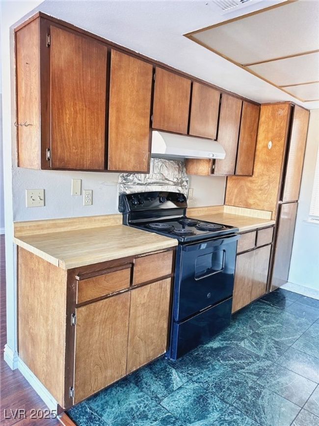 Kitchen featuring electric range, ventilation hood, light countertops, baseboards, and brown cabinets | Image 5