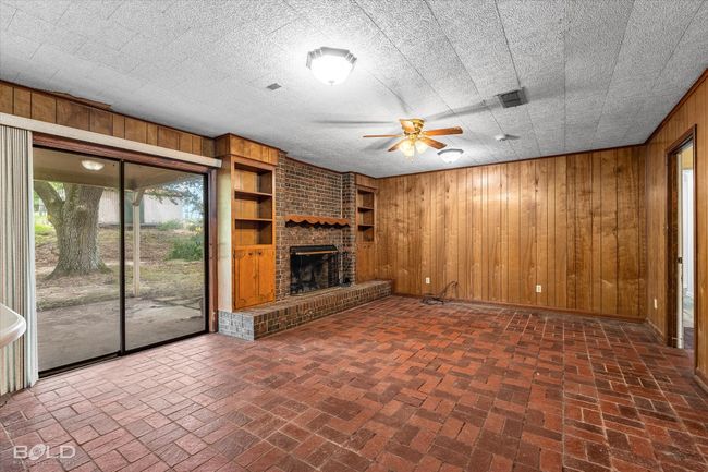 Unfurnished living room with wood walls, brick flooring, ceiling fan, and a brick fireplace | Image 9