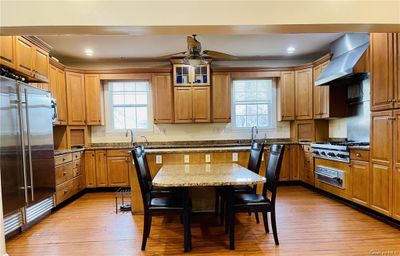 Kitchen with light wood-type flooring, stone counters, ceiling fan, wall chimney exhaust hood, and appliances with stainless steel finishes | Image 2