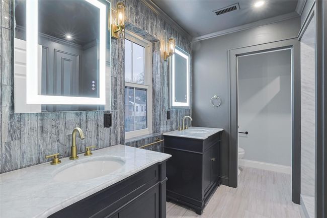 EnSuite full bath with floor to ceiling glass tile accent wall, 2 rustic, high gloss full wood vanities, lighted, anti-fog mirrors, brass fixtures and high grade sconces. | Image 25