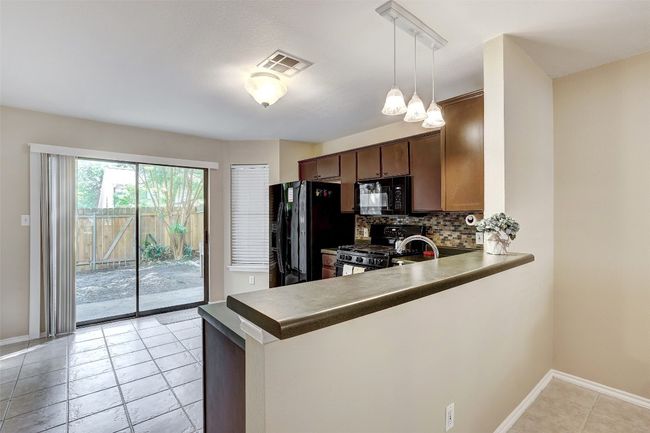 Kitchen with black appliances, a peninsula, decorative backsplash, baseboards, and light tile patterned flooring | Image 14