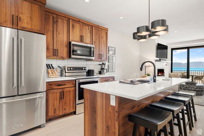 Kitchen featuring appliances with stainless steel finishes, brown cabinets, a sink, light countertops, and open floor plan | Image 42