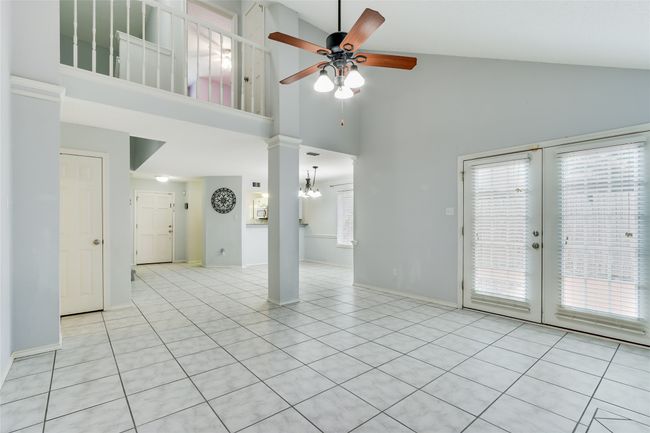 Unfurnished living room featuring light tile patterned floors, french doors, ceiling fan with notable chandelier, high vaulted ceiling, and baseboards | Image 11