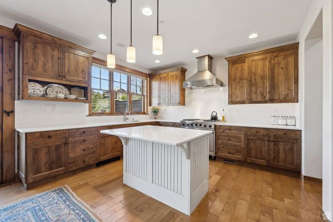 Kitchen featuring wall chimney range hood, a sink, light countertops, high end range, and light wood-type flooring | Image 8