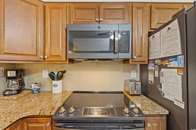Kitchen featuring appliances with stainless steel finishes, brown cabinetry, light stone counters, and a toaster | Image 6