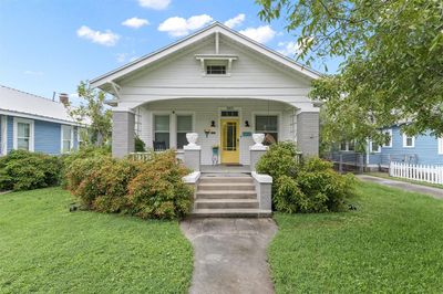 Charming single-story home with a welcoming yellow door, featuring a covered front porch. The property includes a well-maintained lawn and mature landscaping, offering a cozy, neighborly vibe. | Image 1