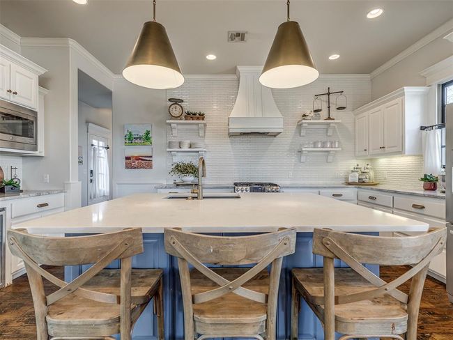 Kitchen with a sink, white cabinets, custom exhaust hood, open shelves, and stainless steel microwave | Image 5