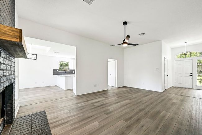 Unfurnished living room featuring wood finished floors, healthy amount of natural light, a brick fireplace, and ceiling fan | Image 9