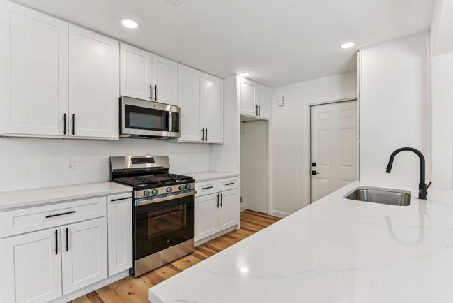 Kitchen featuring stainless steel appliances, white cabinets, light wood-type flooring, light stone counters, and recessed lighting | Image 10