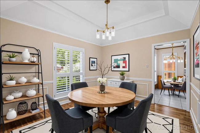 Dining space with a chandelier, wood finished floors, a tray ceiling, crown molding, and wainscoting | Image 5