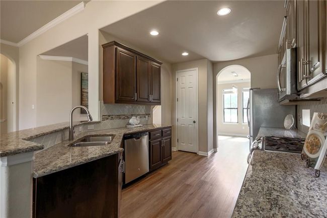 Kitchen with appliances with stainless steel finishes, arched walkways, light wood-style floors, ornamental molding, and light stone countertops | Image 11