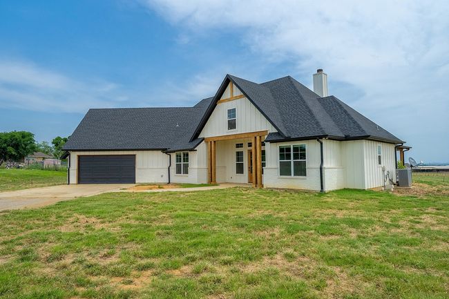 Modern inspired farmhouse featuring a chimney, central AC unit, a garage, concrete driveway, and a shingled roof | Image 4