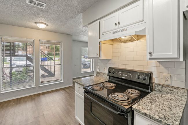 Kitchen featuring black range with electric stovetop, under cabinet range hood, backsplash, white cabinetry, and a textured ceiling | Image 11