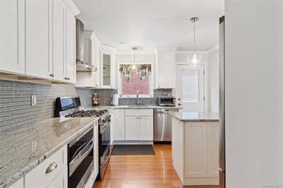 Kitchen with white cabinetry, wall chimney exhaust hood, appliances with stainless steel finishes, and light wood-type flooring | Image 2