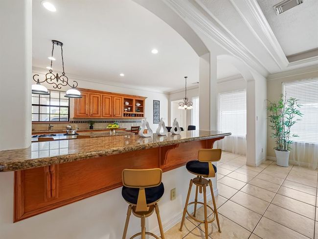 This photo showcases a bright, open-concept kitchen with granite countertops and elegant lighting. The kitchen has warm wooden cabinets and large windows, providing ample natural light. | Image 31