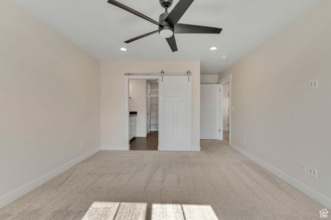 Unfurnished bedroom featuring a barn door, carpet, recessed lighting, a walk in closet, and ceiling fan | Image 16