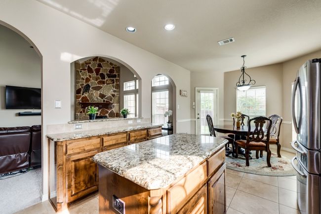 Kitchen with freestanding refrigerator, light stone countertops, open floor plan, recessed lighting, and brown cabinets | Image 15