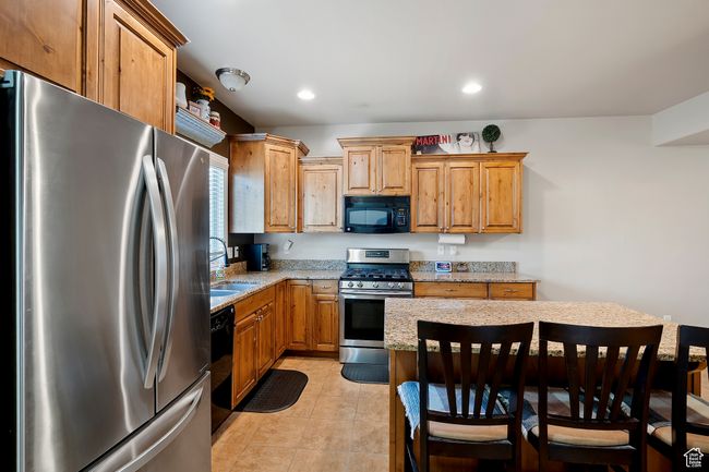 Kitchen featuring black appliances, light stone counters, a breakfast bar, recessed lighting, and light tile patterned floors | Image 9