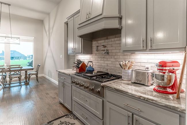 Kitchen with ceiling fan, light hardwood / wood-style flooring, a fireplace, hanging light fixtures, and a kitchen island with sink | Image 10