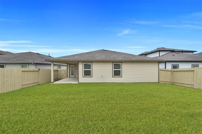 This photo shows a cozy single-story home with a fenced backyard, featuring a covered patio and a neatly maintained lawn, ideal for outdoor activities. | Image 24