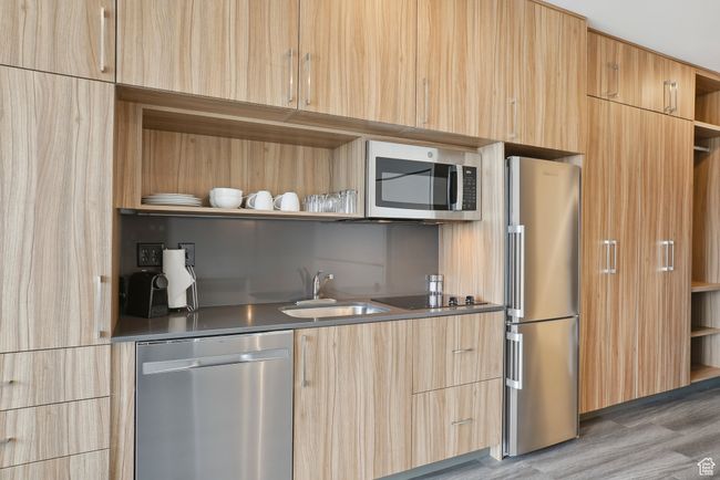 Kitchen with light brown cabinetry, stainless steel appliances, open shelves, and a sink | Image 8