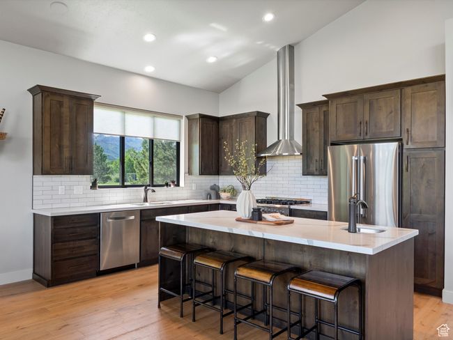 Kitchen with appliances with stainless steel finishes, ventilation hood, a sink, dark brown cabinets, and backsplash | Image 15