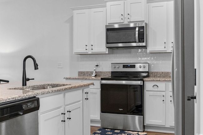 Kitchen with white cabinets, stainless steel appliances, tasteful backsplash, a sink, and light stone counters | Image 11