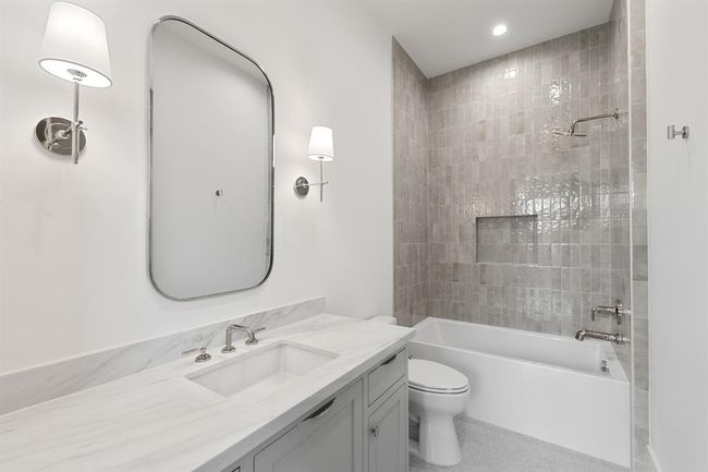 This secondary bath combines practicality with elegance, featuring a beautifully tiled tub-shower combo. The clean lines of the modern fixtures and soft neutral tones create a serene retreat, while designer tile adds texture and sophistication to the space. It’s a perfect blend of comfort and style for everyday use. | Image 33