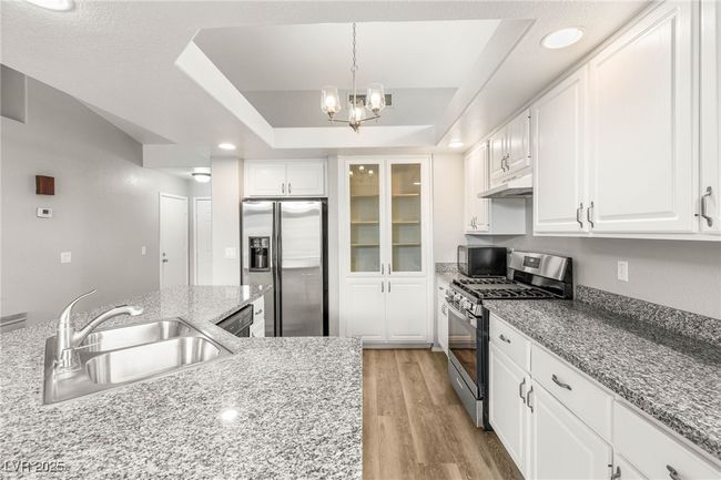 Kitchen featuring white cabinets, a sink, light wood-style floors, under cabinet range hood, and appliances with stainless steel finishes | Image 10
