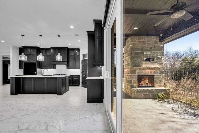 Kitchen with light countertops, a center island with sink, a sink, ceiling fan, and an outdoor stone fireplace | Image 18