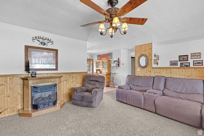Living room with wood walls, a ceiling fan, wainscoting, carpet floors, and a textured ceiling | Image 6