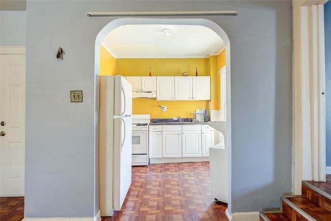 Kitchen with white appliances, under cabinet range hood, arched walkways, white cabinetry, and crown molding | Image 30