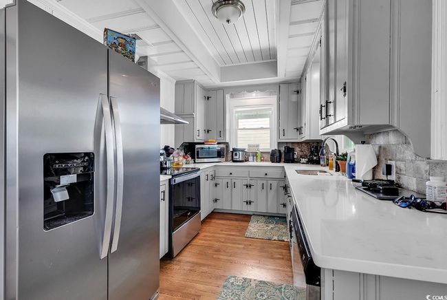 Kitchen featuring sink, backsplash, a tray ceiling, stainless steel appliances, and light wood-type flooring | Image 13