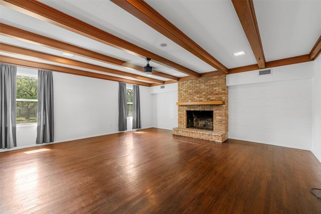 Unfurnished living room with a brick fireplace, plenty of natural light, wood finished floors, and beam ceiling | Image 9