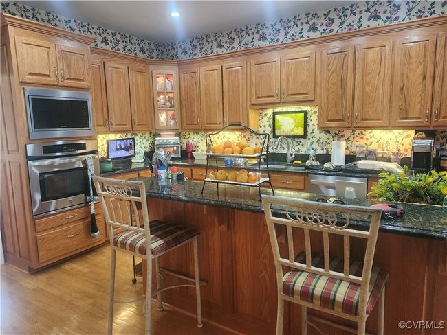 Kitchen with a kitchen bar, dark stone countertops, stainless steel appliances, and light wood finished floors | Image 6