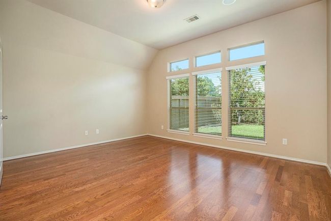 Tucked away at the back of the home for added privacy, this spacious primary suite offers a peaceful retreat. A stunning wall of windows fills the room with natural light and provides a view of the backyard. The room features warm wood flooring, high ceilings, and direct access to a luxurious ensuite bathroom—complete with a soaking tub, separate shower, and generous walk-in closet. | Image 18