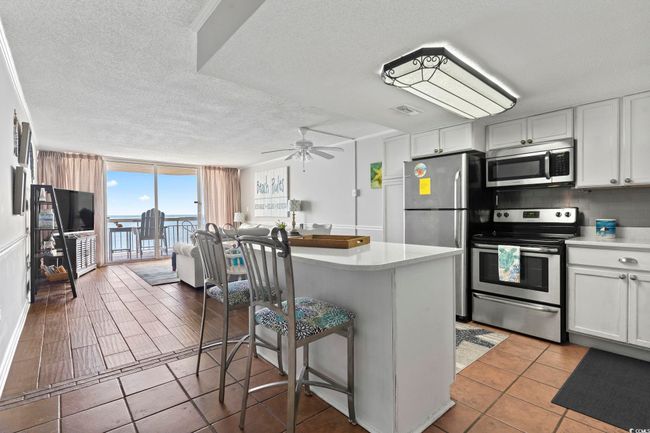 Kitchen featuring decorative backsplash, ceiling fan, a kitchen bar, appliances with stainless steel finishes, and expansive windows | Image 13