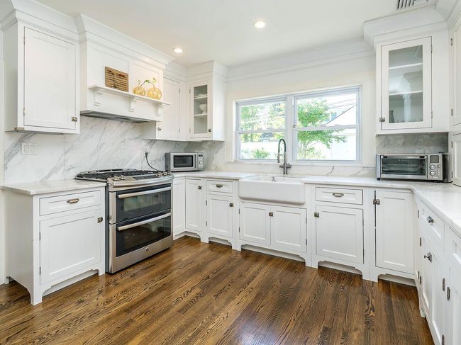 Kitchen with stainless steel appliances, a sink, white cabinets, decorative backsplash, and dark wood-type flooring | Image 9