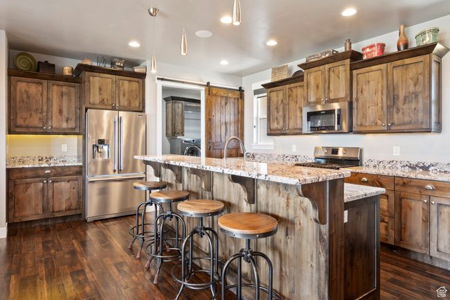 Kitchen with a kitchen breakfast bar, light stone counters, stainless steel appliances, a center island with sink, and dark wood-style floors | Image 10