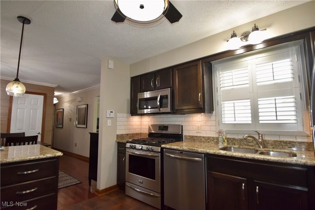 Kitchen with stainless steel appliances, a sink, decorative backsplash, dark brown cabinets, and baseboards | Image 12