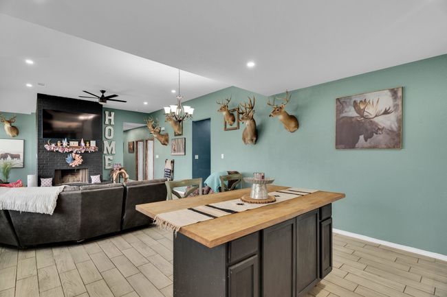 Kitchen with wooden counters, wood tiled floors, a brick fireplace, a center island, and baseboards | Image 7
