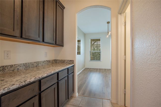 Kitchen with dark brown cabinets, arched walkways, light wood-type flooring, and light stone countertops | Image 16