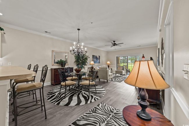 Dining space featuring wood finished floors, a ceiling fan, crown molding, a chandelier, and baseboards | Image 5