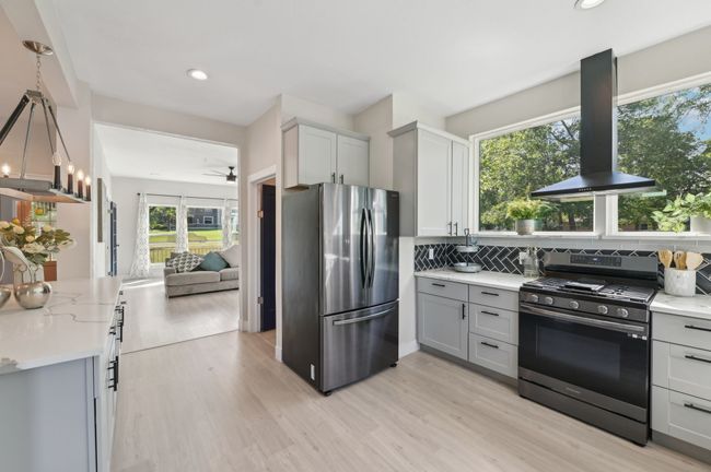 Kitchen with appliances with stainless steel finishes, island exhaust hood, gray cabinetry, decorative backsplash, and light wood-type flooring | Image 15