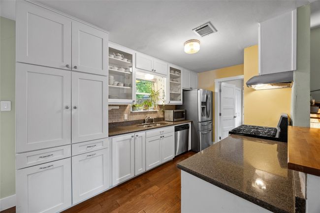 Kitchen with dark wood-type flooring, glass insert cabinets, white cabinets, backsplash, and appliances with stainless steel finishes | Image 6