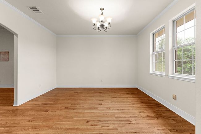 Empty room with light wood-style floors, visible vents, an inviting chandelier, and ornamental molding | Image 18
