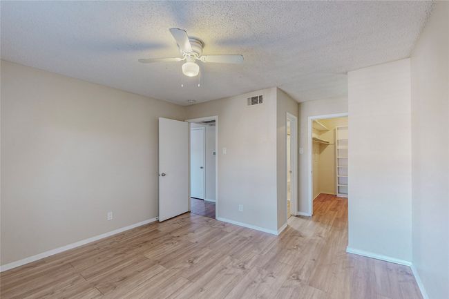 A vacant bedroom with polished hardwood floors, a ceiling fan and a walk-in closet with shelves offering a bright and open feel. | Image 18
